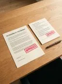 Two printed documents on a wooden desk with red APPROVED stamps and a pen.