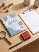 Holzschreibtisch mit Notizbuch "Digital Strategy", Checklisten-Klemmbrett, rotem Häkchenstempel und Lupe.