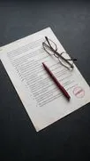 Bedrucktes Dokument mit rotem APPROVED-Stempel, dunkelrotem Stift und Lesebrille darauf.