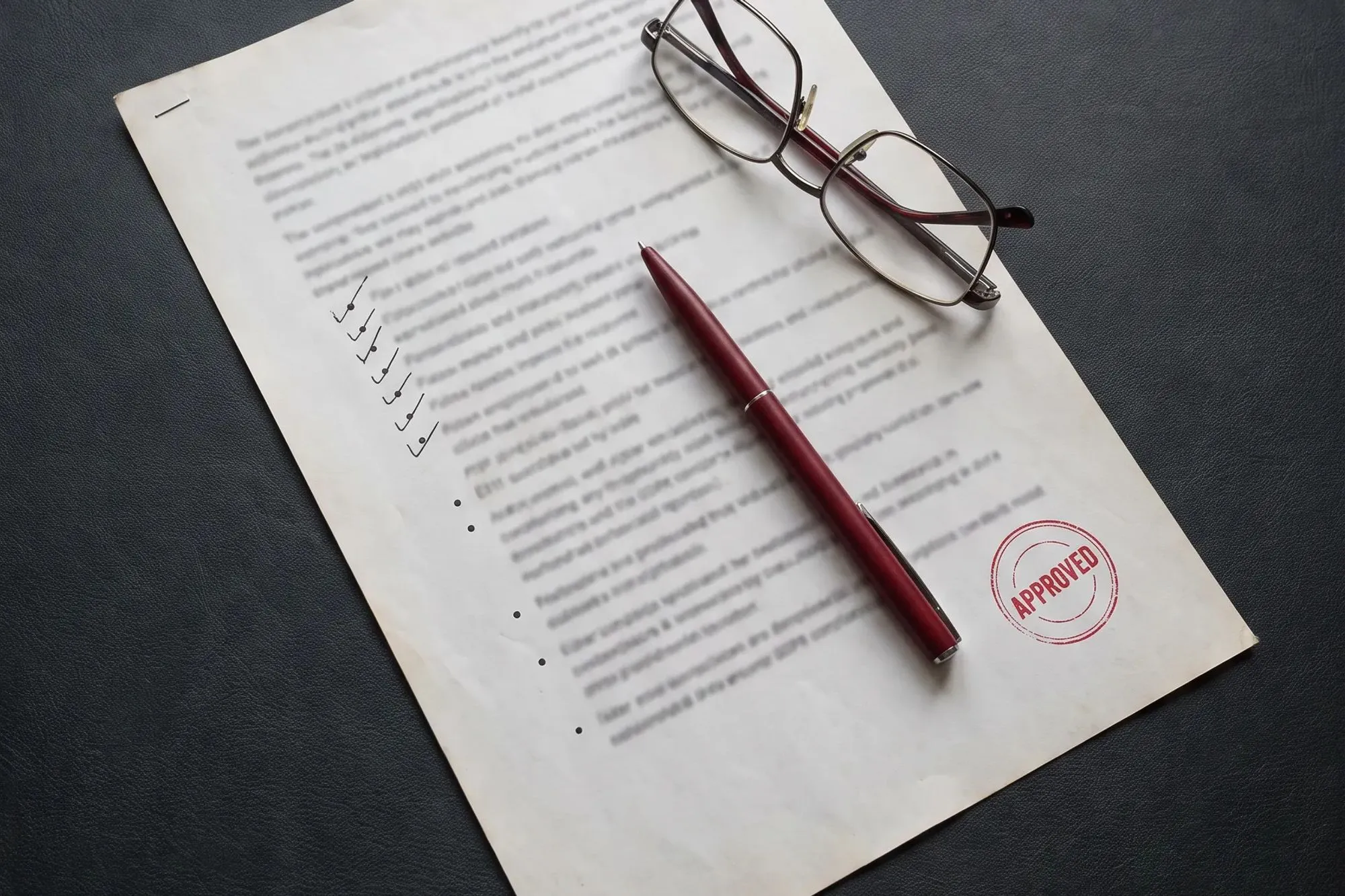 Bedrucktes Dokument mit rotem APPROVED-Stempel, dunkelrotem Stift und Lesebrille darauf.