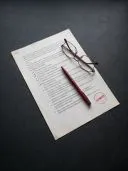 Bedrucktes Dokument mit rotem APPROVED-Stempel, dunkelrotem Stift und Lesebrille darauf.